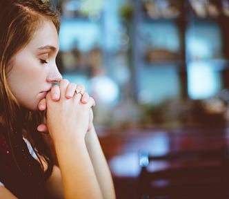 Woman holding her hands together with eyes closed. Looks like she is meditating or praying.