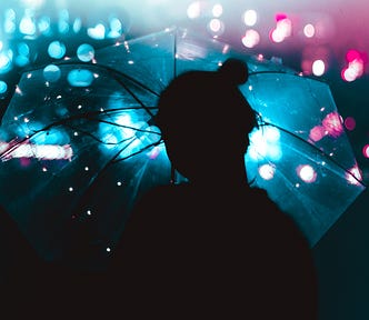 Person silhouetted beneath a clear umbrella. There’s arty purple and blue lighting in the background.