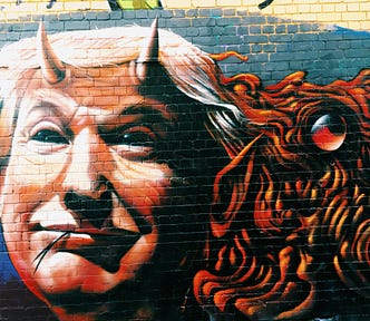Graffiti painting of Donald Trump sporting horns and a forked tongue on a blue brick wall.