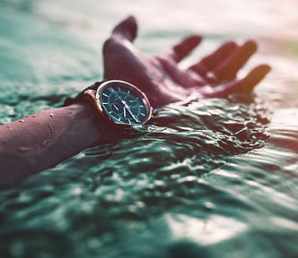 A white lower left arm and hand face upwards. The person wears an upward-facing wristwatch, with the arm, hand, and watch barely dipping into a body of water. Lifestyle (including diet and exercise) changes epigenetics, slowing aging.