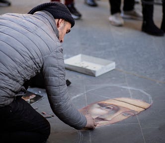 A street artist recreating the mona lisa in colored chalk on a grey tiled sidewalk with great likeness.