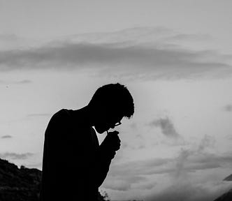 A silhouette of a person lighting a cigarette and looking down a mountain.