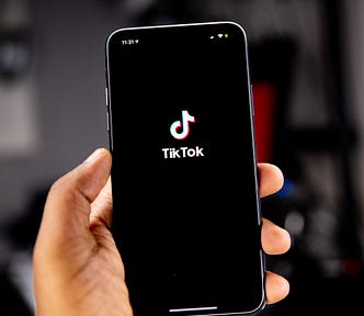 A hand holding up a phone where the screen is black, except for the white TikTok logo