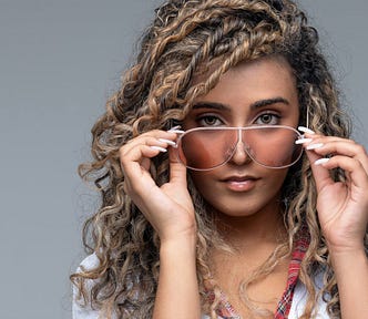 Studio portrait of an attractive and hip young woman with curly hair and sunglasses looking into the camera confidently