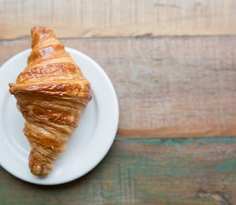 A croissant on a small white plate on a a wooden counter top.
