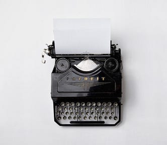 Black vintage Adler ‘Favorit’ typewriter with a blank page against a blank white background.