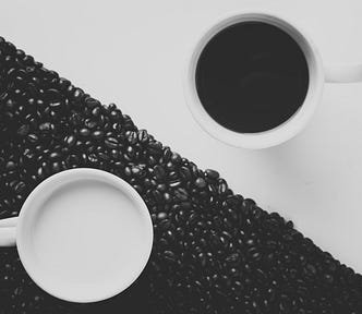 An image showing two mugs, one with black coffee on a white BG. And another one with milk on a BG of coffee beans. It symbolizes yin-yang.