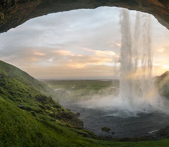 The view of a broad landscape from behind a waterfall at dawn.