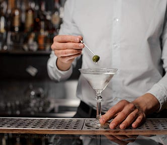 A bartender holding an olive over a martini.