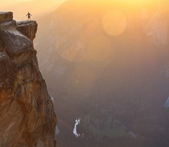 person standing on a mountain peak staring into the valley and sun