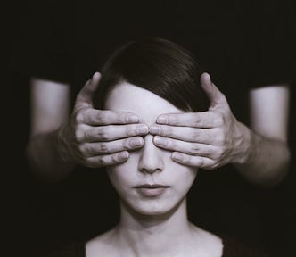 a woman sitting while a man behind her covers her eyes with his hands