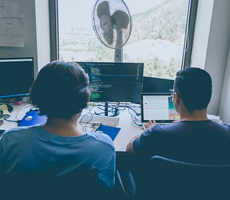 Two programmers sitting next to each other in the office in a hot day and discusses their code