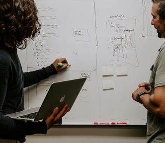 a man and woman writing schematics on a whiteboard