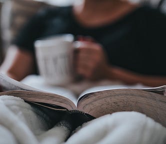 Person reading a book with a cup of coffee in hand.