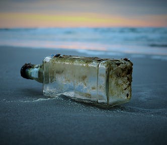 A dirty, empty, abandoned glass bottle lies on a beach at sunrise/sunset