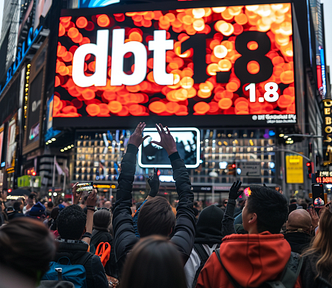 Enthusiastic crowd raising their hands and taking photos with their phones in front of an illuminated billboard in Times Square, featuring the announcement ‘dbt 1.8’ with glowing, festive lights.
