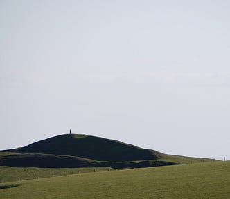 green, grassy hill, small fence, empty blue sky