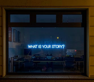 window with luminous sign that says “what is your story”