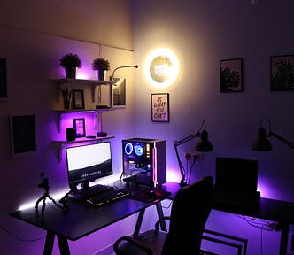 dark room lit by purple light of a desktop computer set up for editing youtube videos.