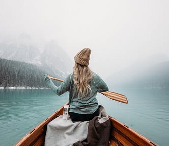 women paddles canoe across wintery lake
