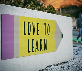 a rectangle sign with a large pencil on it. the pencil says Love to Learn