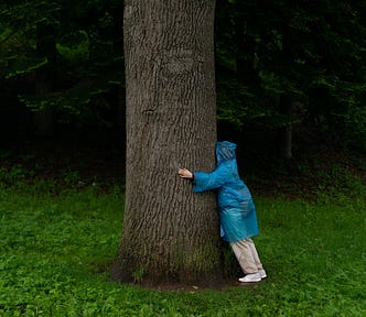 Woman wearing a blue raincoat hugging a tree.