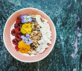 A delicious bowl of coconut, seeds, raspberries, plant milk, and viola flowers for decoration