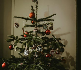 A spindly, sparse real Christmas tree with red bulb ornaments and gold snowflake ornaments.