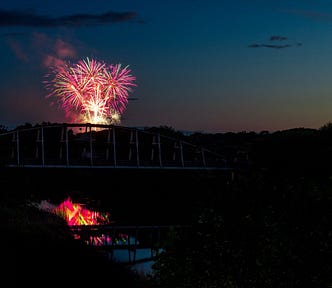 Fireworks exploding over river with bridge