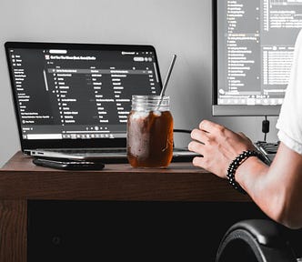 a software engineer sitting on his disk and work with 2 screens and a cold dark drink
