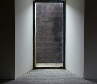 An uninviting door that is also a brick wall. An unwelcoming hallway, all in monochromatic shades of black, white and grey.