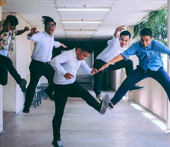 Five people jumping into the air whilst in a school corridor.