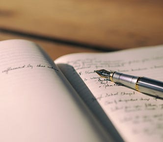 A photograph of an open notebook with a fountain pen resting on the page.
