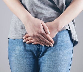 woman stands holding hands over lower abdomen