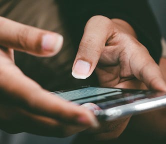 Closeup of 2 hands holding a cell phone with the thumbs poised to test a message