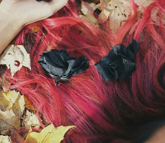 Red haired woman lying on leaves holding black roses