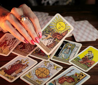 Tarot cards lie on a table and a hand holds up a tarot card.