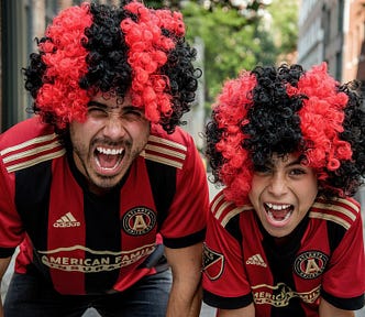 father and son in matching wigs and football jerseys cheering