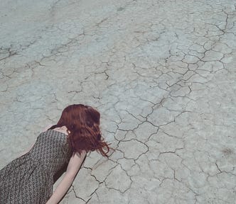 Woman with hair covering her face lying on dry, cracked ground