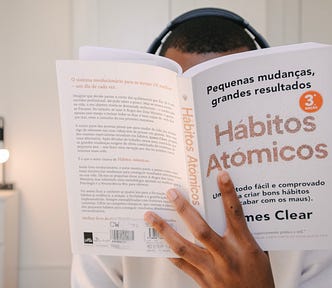 Man reading Atomic Habits (Atomics Habitos) in Spanish. his face is hidden behind the book and he is wearing big headphones.