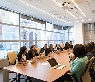 a meeting room full of people with laptops on a long table