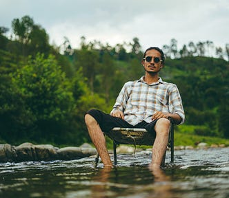 A man practising Loving Kindness Mindfulness sat in a chair in a stream outside in nature.