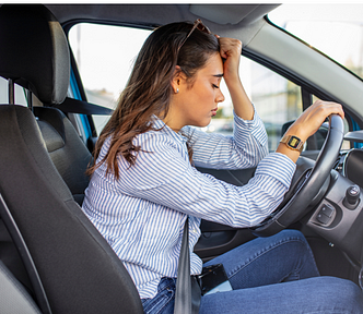 Woman sitting in her car with her eyes closed and her fist to her forehead.