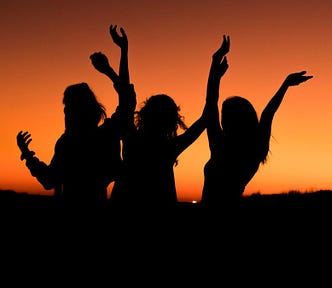 three women dancing in with an orange sky in the background