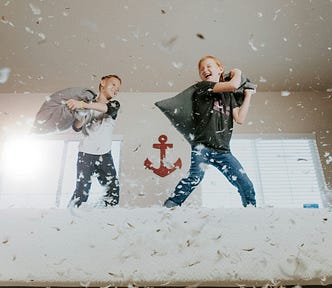 Tow boys pillow-fighting on a bed with feathers flying.