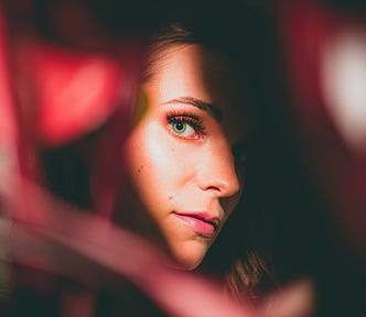 A woman peeks out from some blurry red foliage, one piece of which is heart-shaped