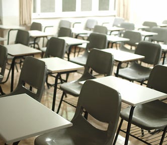 The picture shows a classroom full of empty desks and chairs, awaiting the students.