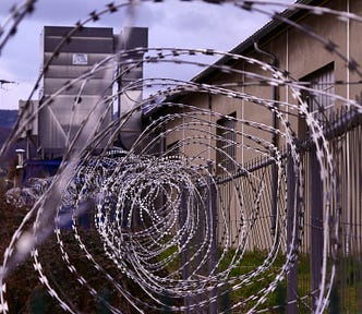 Barbed wire fence with high walls behind it.