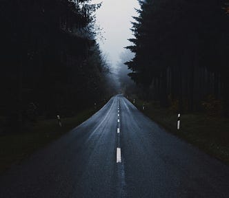 A dark, empty road at night with tall trees on both sides
