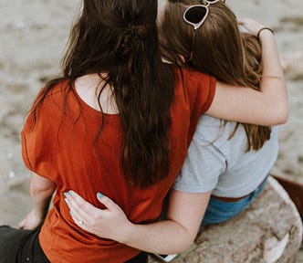 Two women, sitting on a log, with their arms around each other.